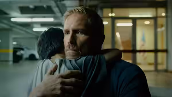 A man embraces another person in a brightly lit institutional hallway