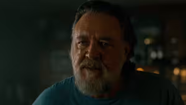 A grey-bearded man in a blue shirt looks across a dim room