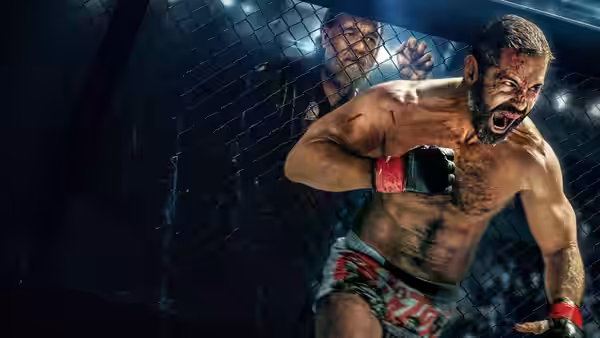 A bare-chested fighter in red gloves lunges inside a fenced cage