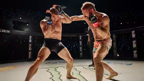 Two bare-chested fighters spar on a marked arena floor
