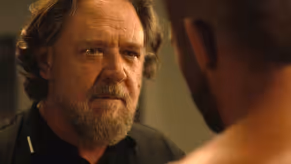 A bearded man in a dark shirt faces someone across a room