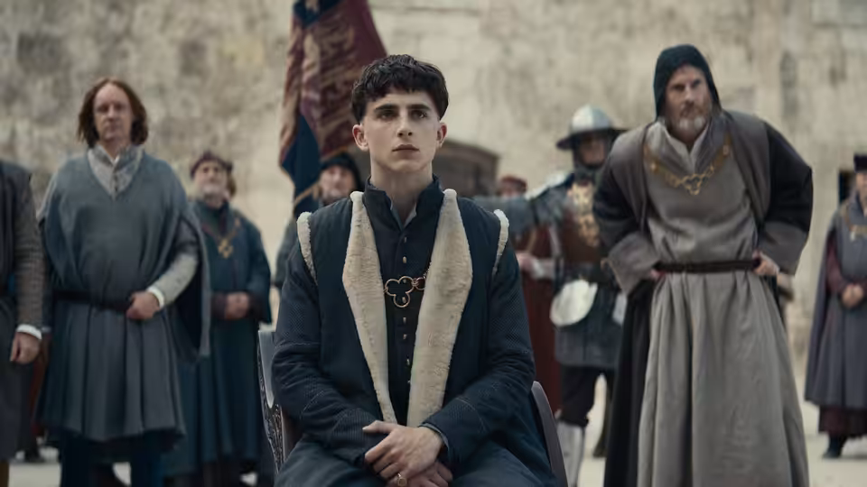 Hal (Timothée Chalamet) stands among clerics and attendants in a pale stone hall