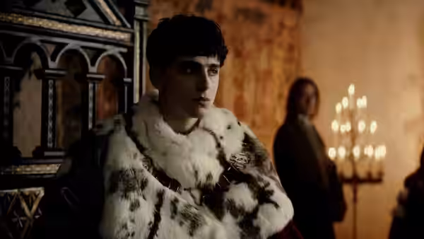 Hal (Timothée Chalamet) wears a fur-trimmed robe in a candlelit palace room