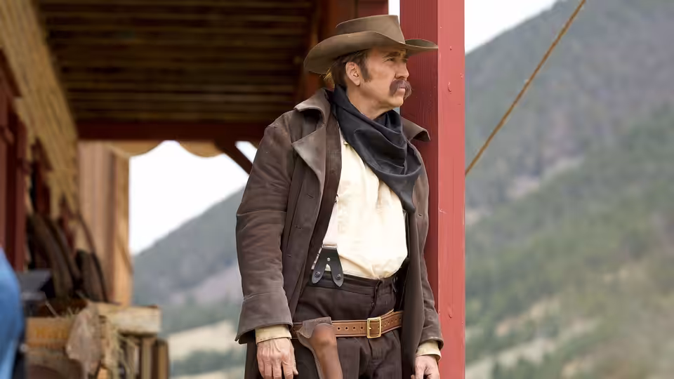 Colton Briggs (Nicolas Cage) stands in a doorway wearing a long coat and cowboy hat