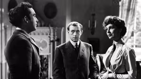 Dennis Price as Louis Mazzini stands between a man and a woman in a room