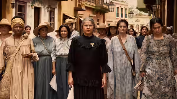 Several women in long dresses stand together on a town street