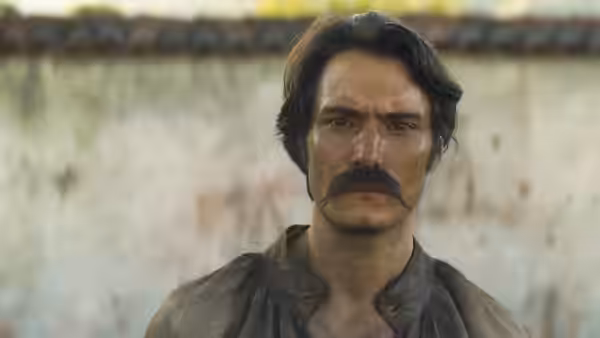 A mustached man in a dark shirt looks ahead