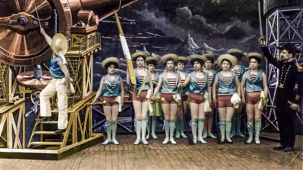 A row of sailors stands at attention beside a telescope and uniformed officer