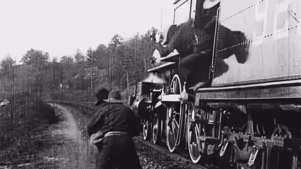 A bandit clambers onto a locomotive as it travels through wooded countryside