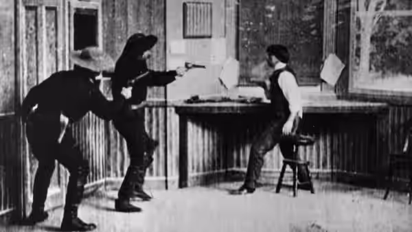 A bandit aims his pistol at a seated telegraph operator inside the station office