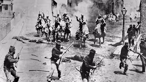 Armed men run through a town as mounted riders approach in the distance