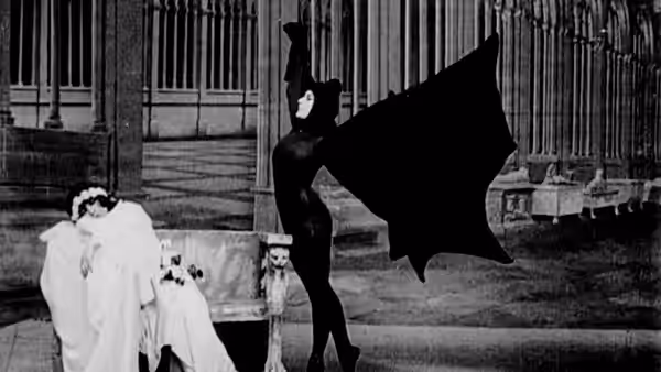 Irma Vep (Musidora) in a black catsuit moves among guests in a grand hall