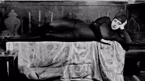 Irma Vep (Musidora) in a black catsuit lies across a bed in a furnished room