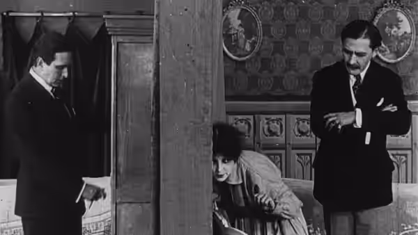 Philippe Guérande (Édouard Mathé) and another man watch a woman crouching behind a pillar
