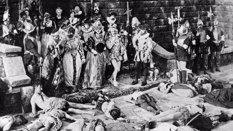 A group of men and women gather around bodies lying across a stone courtyard