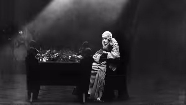 A woman in a head covering sits alone at a table in a dark room