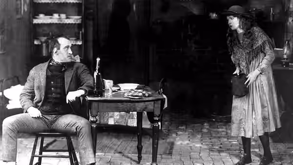 Battling Burrows (Donald Crisp) sits at a table as Lucy Burrows (Lillian Gish) stands nearby