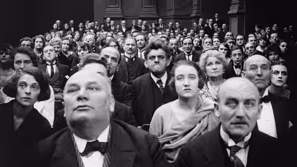 Men and women sit closely packed in an auditorium, facing forward