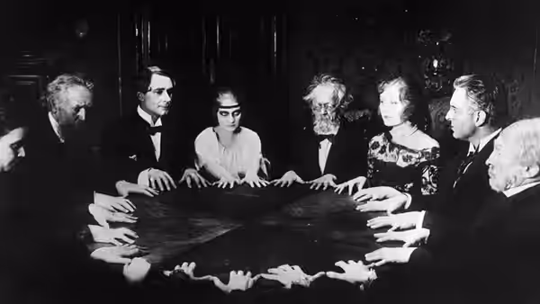 A group gathers around a table, extending their hands toward its center