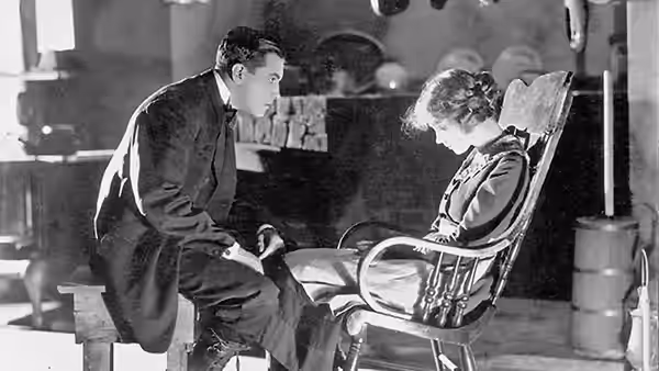A man kneels beside a woman reclining in a chair indoors