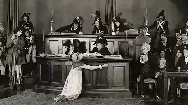 A woman in a white dress pleads before officials seated behind a courtroom bench