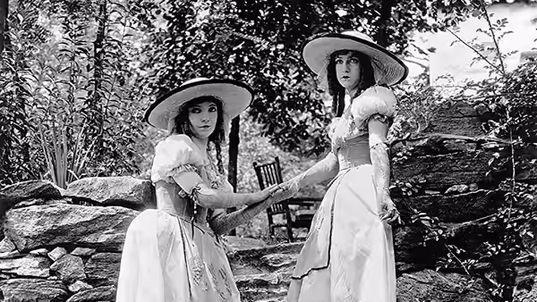 Henriette (Lillian Gish) and Louise (Dorothy Gish) stand in a garden beside a stone wall