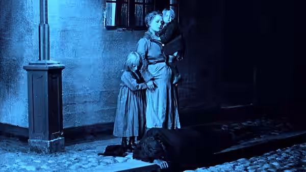 A woman and two girls stand over a prone figure in a dark room