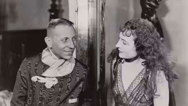 A smiling man in a patterned robe faces a woman by the doorway