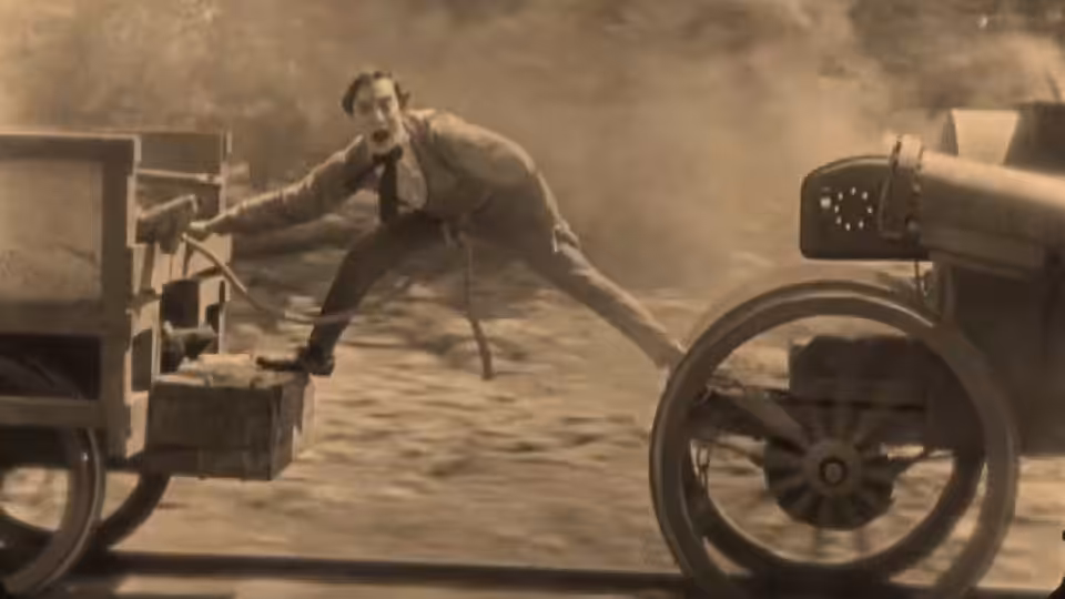 William McKay (Buster Keaton) stretches between the front and rear of a moving automobile