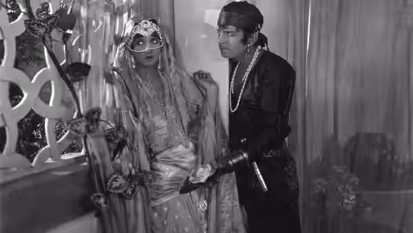 A veiled woman stands beside a man in dark robes inside a palace