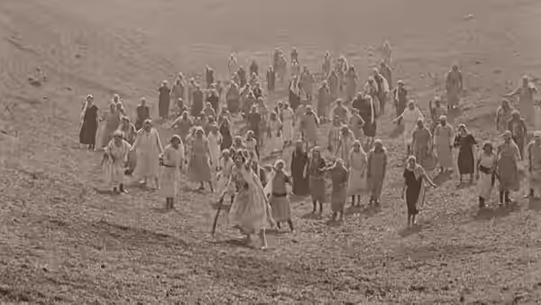 A crowd of women spreads across an open hillside, pursuing a fleeing man