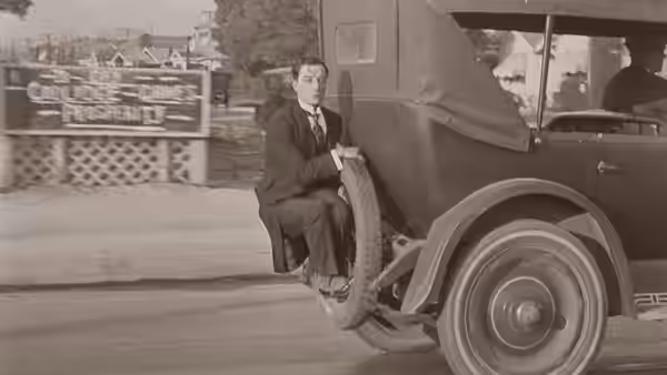 Jimmie Shannon (Buster Keaton) rides on the running board of a moving car
