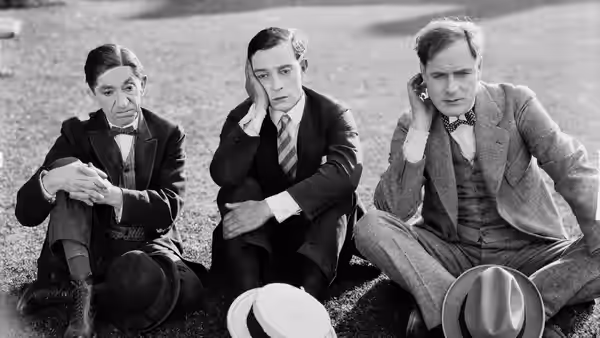 Three formally dressed men sit on the ground, resting their heads in their hands