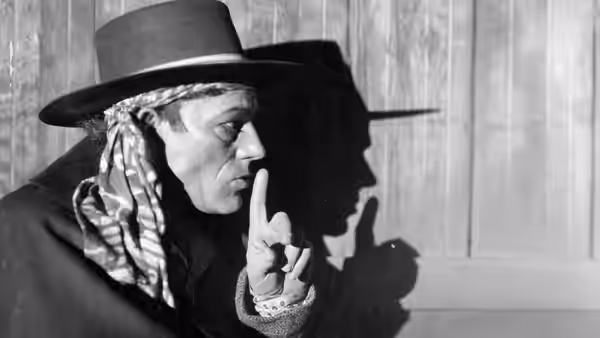 Alonzo (Lon Chaney) in a wide-brimmed hat and headscarf raises a finger beside his shadow