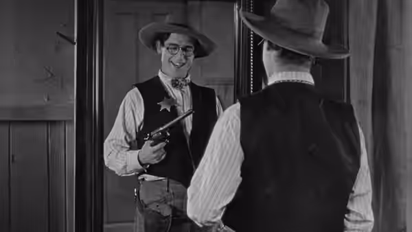 Harold Hickory (Harold Lloyd), wearing a sheriff's star and holding a gun, faces a man in a doorway