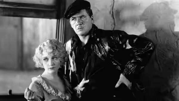 Bill Roberts (George Bancroft) stands beside Mae (Betty Compson) in a room