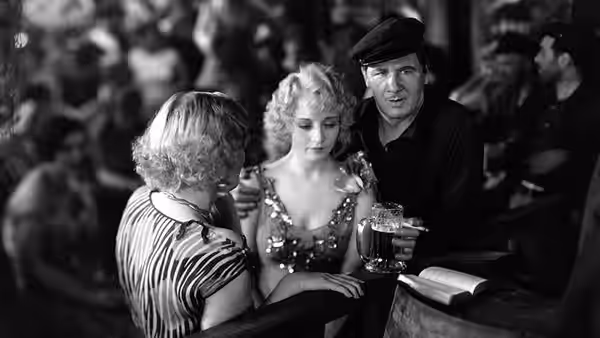 Mae (Betty Compson) sits at a bar with a woman and a man holding a drink
