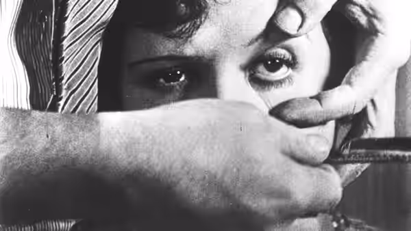 A man holds a razor across a woman's eye