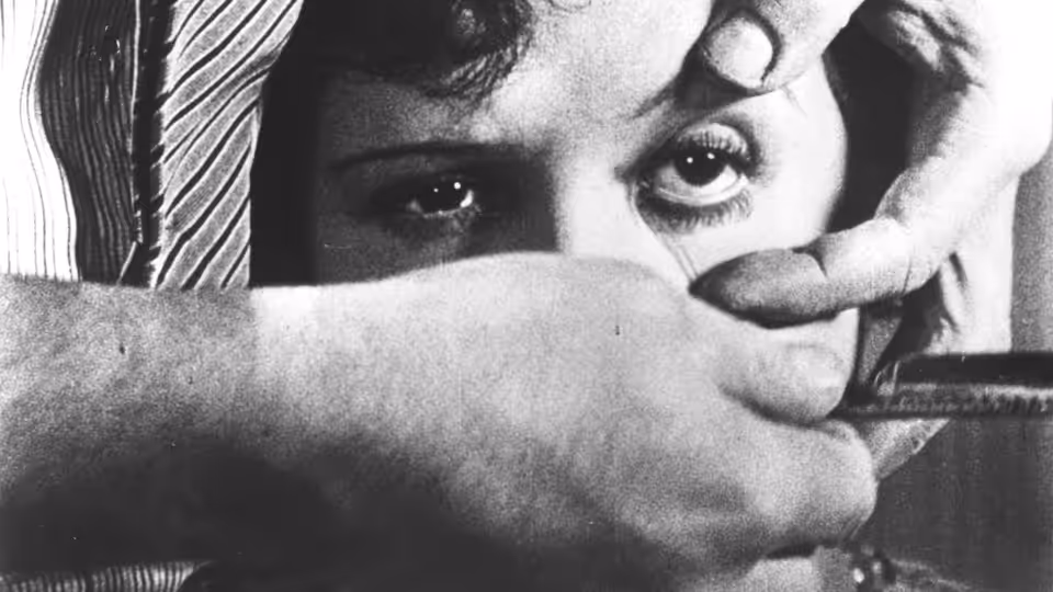 A man holds a razor across a woman's eye