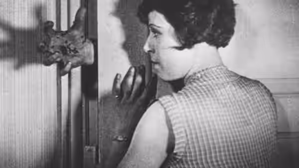 A woman peers through a doorway as a hand reaches toward her