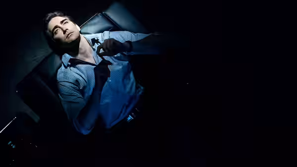 Lee Pace as Joe MacMillan reclines in a chair holding a phone receiver