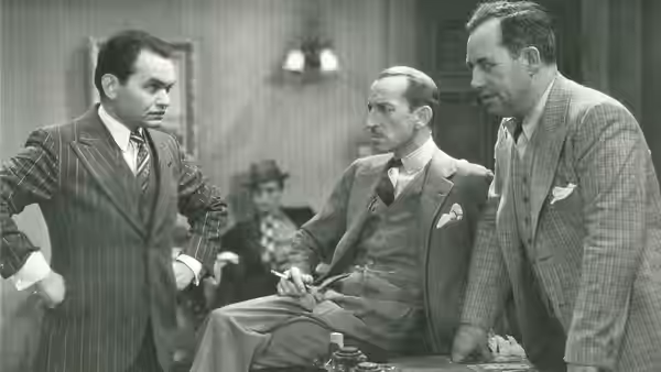 Three suited men gather around a seated man in a pinstriped suit