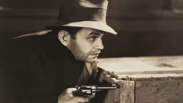 Rico (Edward G. Robinson) crouches behind a wooden counter with a pistol