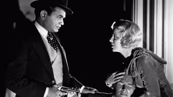 A suited man and a woman stand over another man lying on the floor