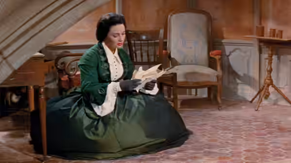 Lola Montes (Martine Carol) reads a letter while seated in a furnished room