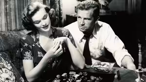 A woman examines jewelry beside a man seated at a table