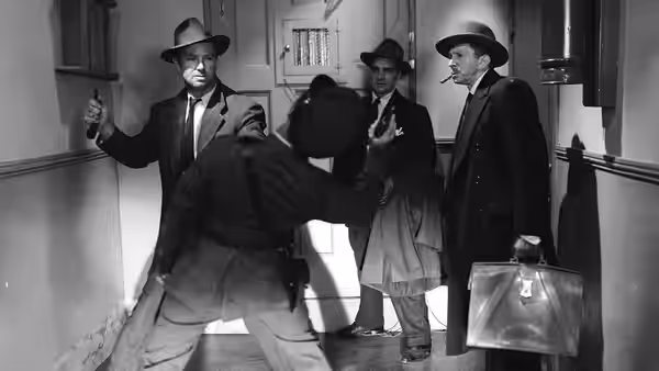 Several suited men gather in a hallway, one holding a suitcase