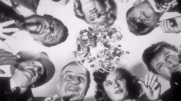 A group gathers around and peers down at an arrangement on a table