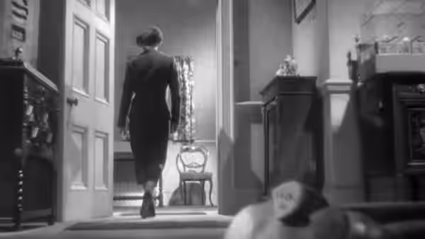 A suited man walks through a doorway as a woman lies in the foreground