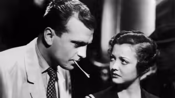 Ted (John Loder) leans toward Mrs. Verloc (Sylvia Sidney) with a cigarette